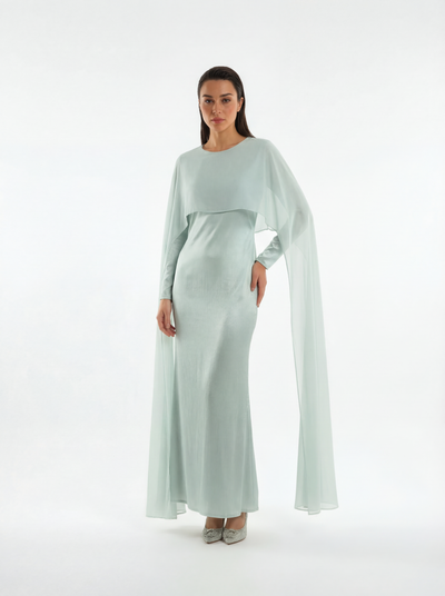 Woman wearing a light mint long-sleeve dress with a cape on a white background