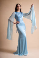 Mariya aquatic blue modest evening gown — editorial pose with a raised arm and flowing shimmering cape sleeve, Mystic Modesty