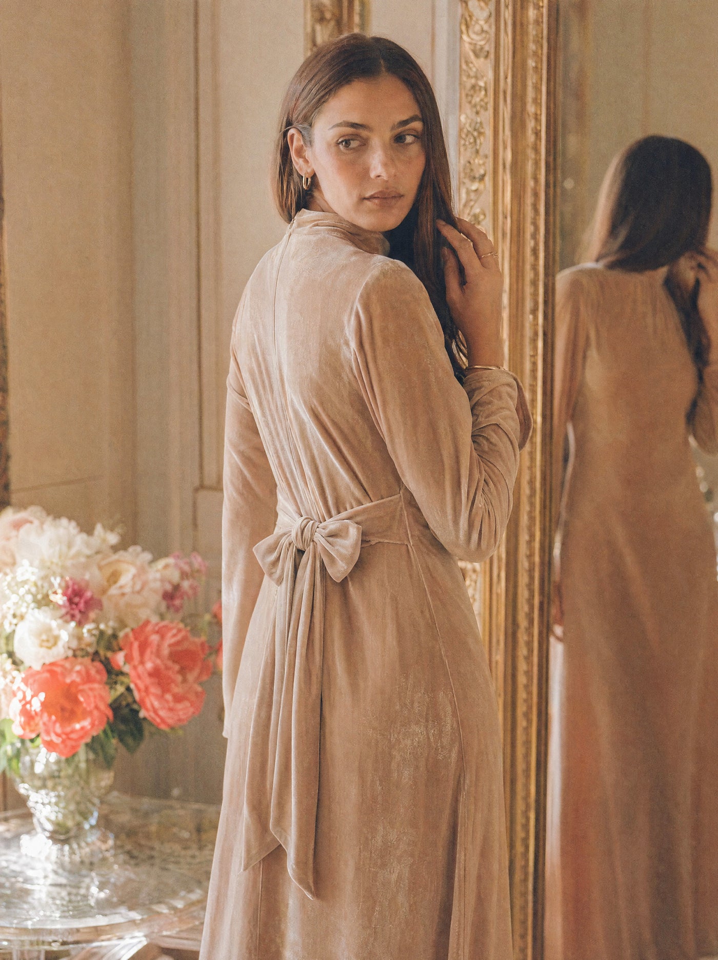 Mystic Modesty SS26— Camille Warm Beige velvet gown, intimate dressing-room moment with gilded mirror reflection, modest evening wear, Vogue editorial film aesthetic