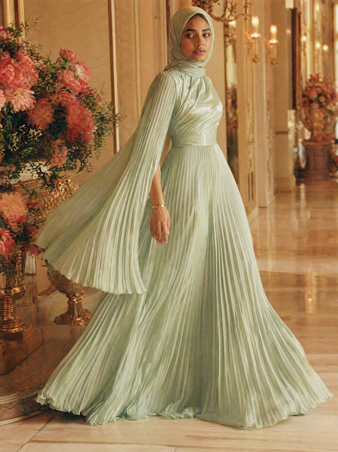 Mystic Modesty SS26— Saffira Mint pleated satin, sunlit palatial corridor mid-stride with rose-gold sconces, modest evening wear, Vogue editorial film aesthetic